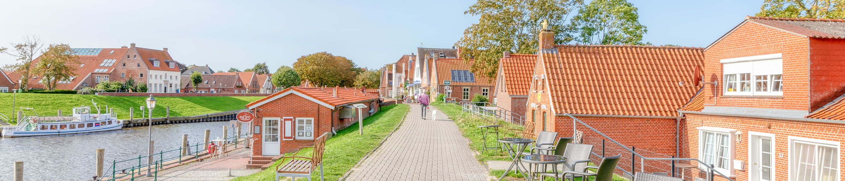 Spaziergänger mit Hund entlang der Häuser am Deich in Greetsiel