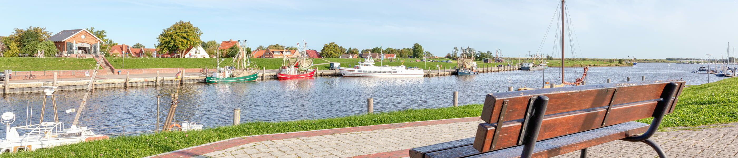 Hafen in Greetsiel mit Booten und Sitzbank im Vordergrund