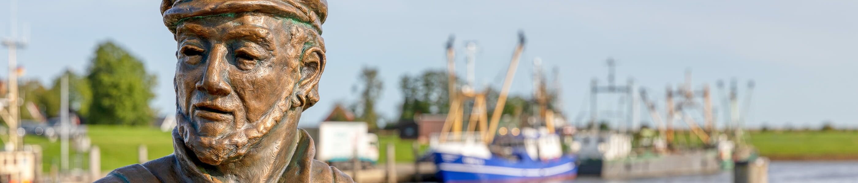 Fischerfigur in Greetsiel mit Hafen und Booten im Hintergrund
