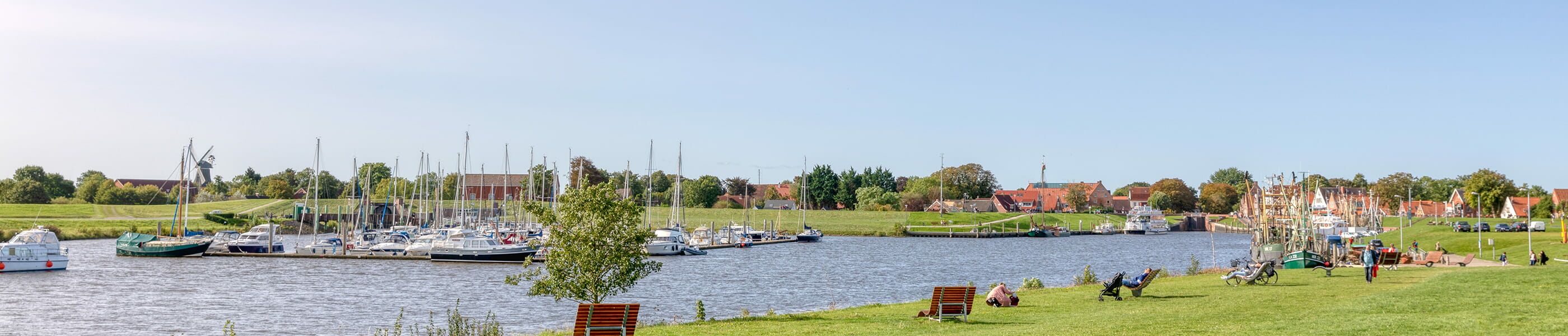 Segelboote im Hafen von Greetsiel mit Wiese und Sitzbänken