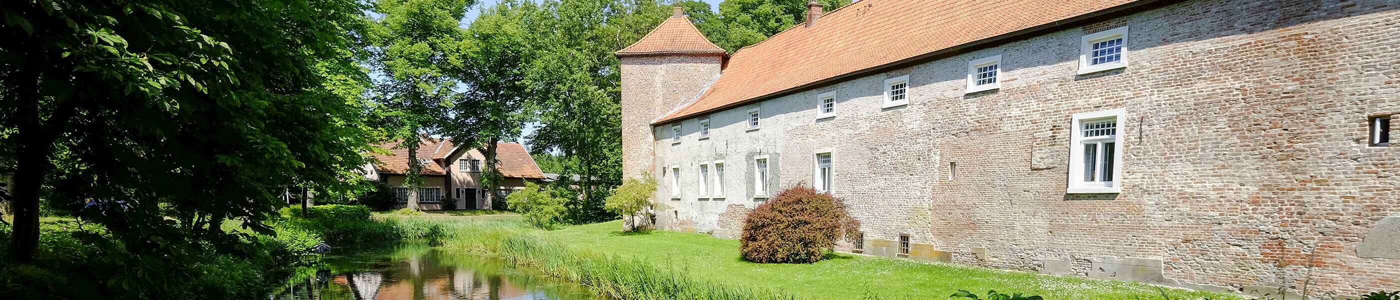 Historisches Gebäude in Hage mit Wassergraben und Bäumen