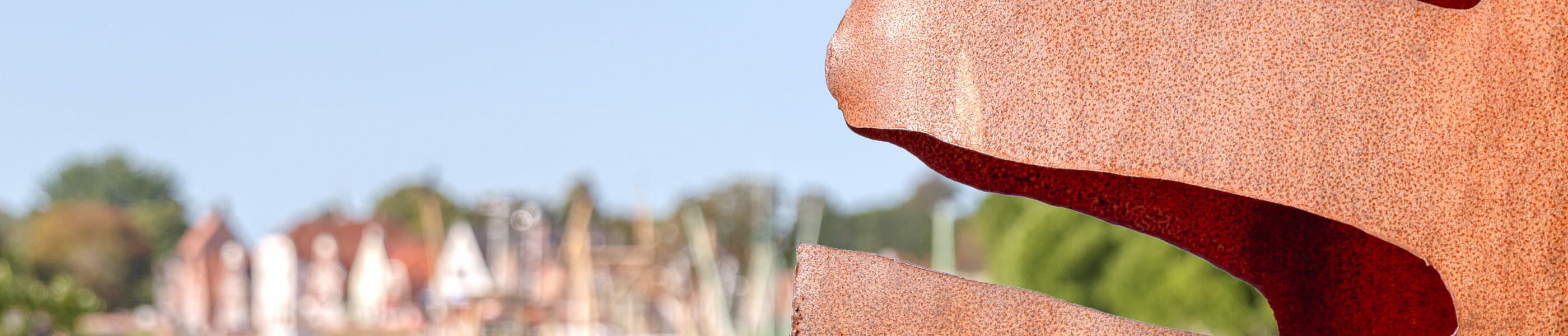 Skulptur im Vordergrund mit unscharfem Hafen in Greetsiel